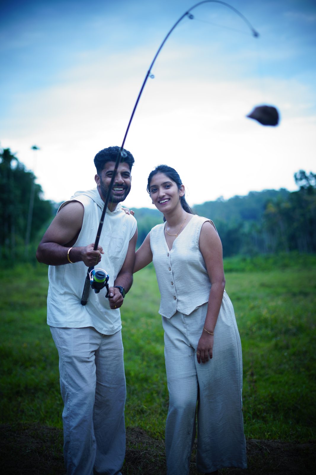 A couple holding a fishing rod on the grass at dusk